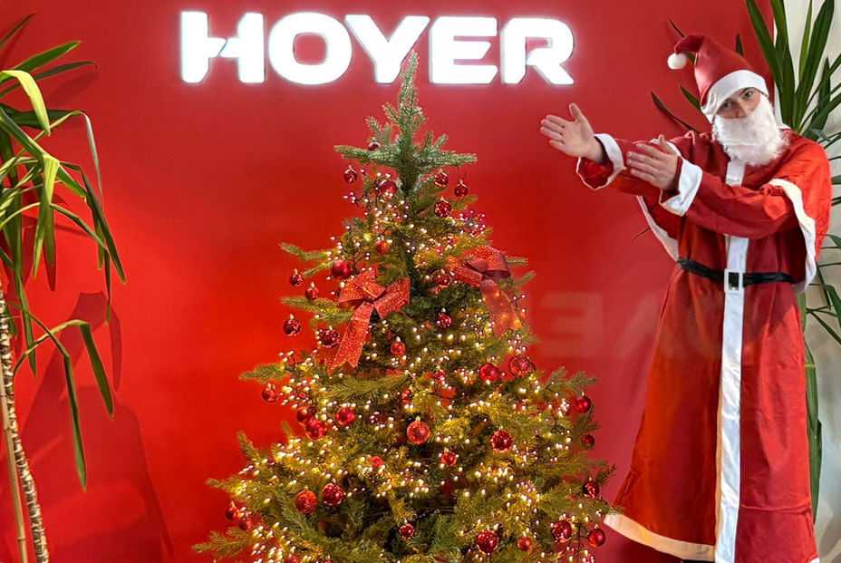 Hoyer Hintergrund mit Weihnachtsmann der auf Weihnachtsbaum zeigt